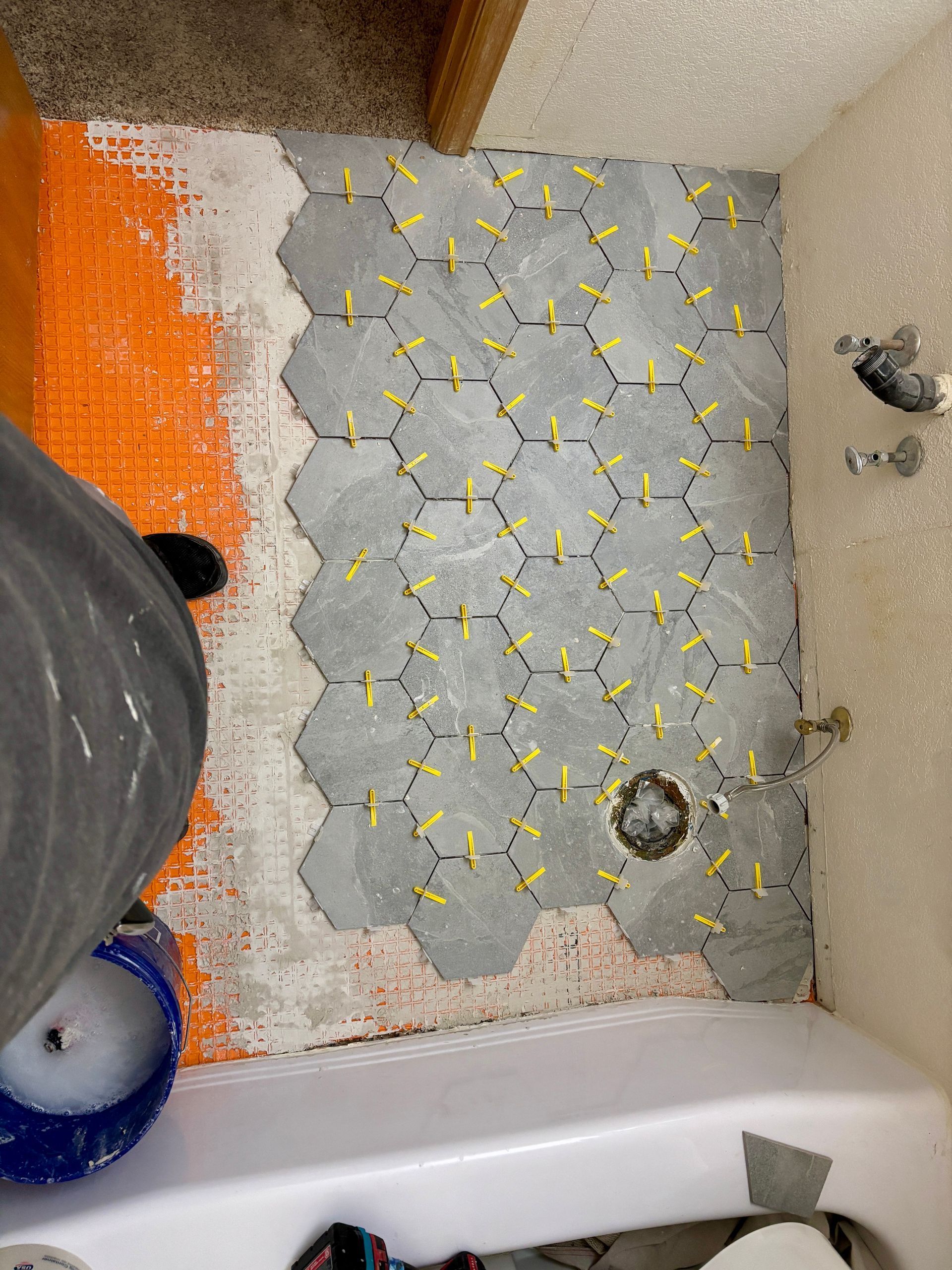 Bathroom floor tiling in progress: gray hexagon tiles with yellow spacers