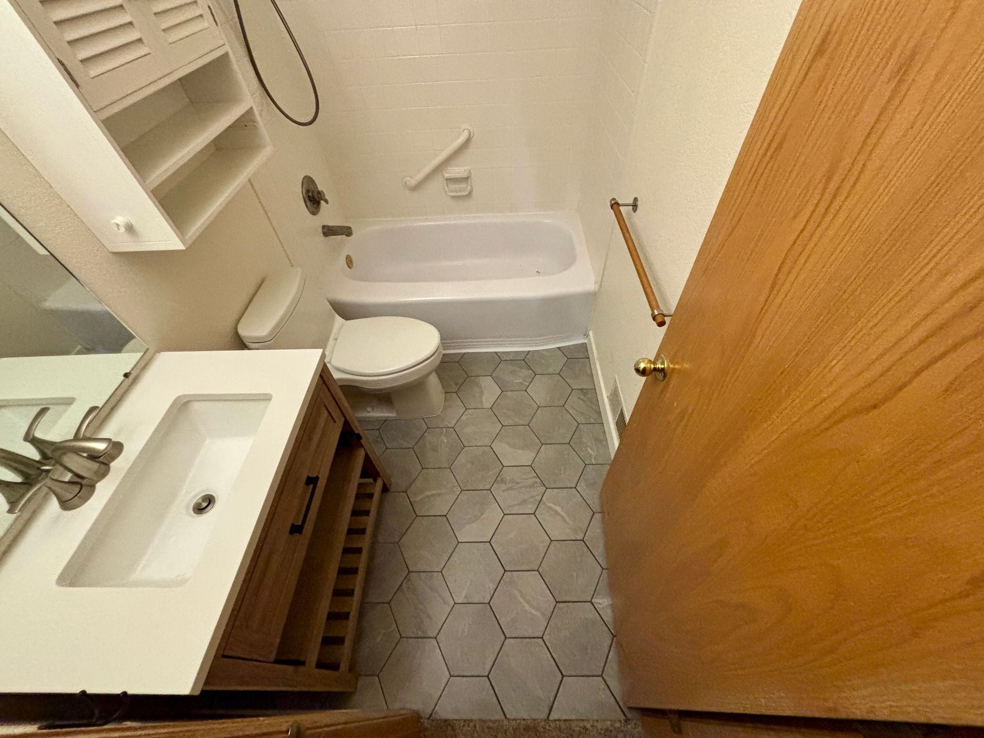 Bathroom with white tub, toilet, vanity, and honeycomb tile floor.