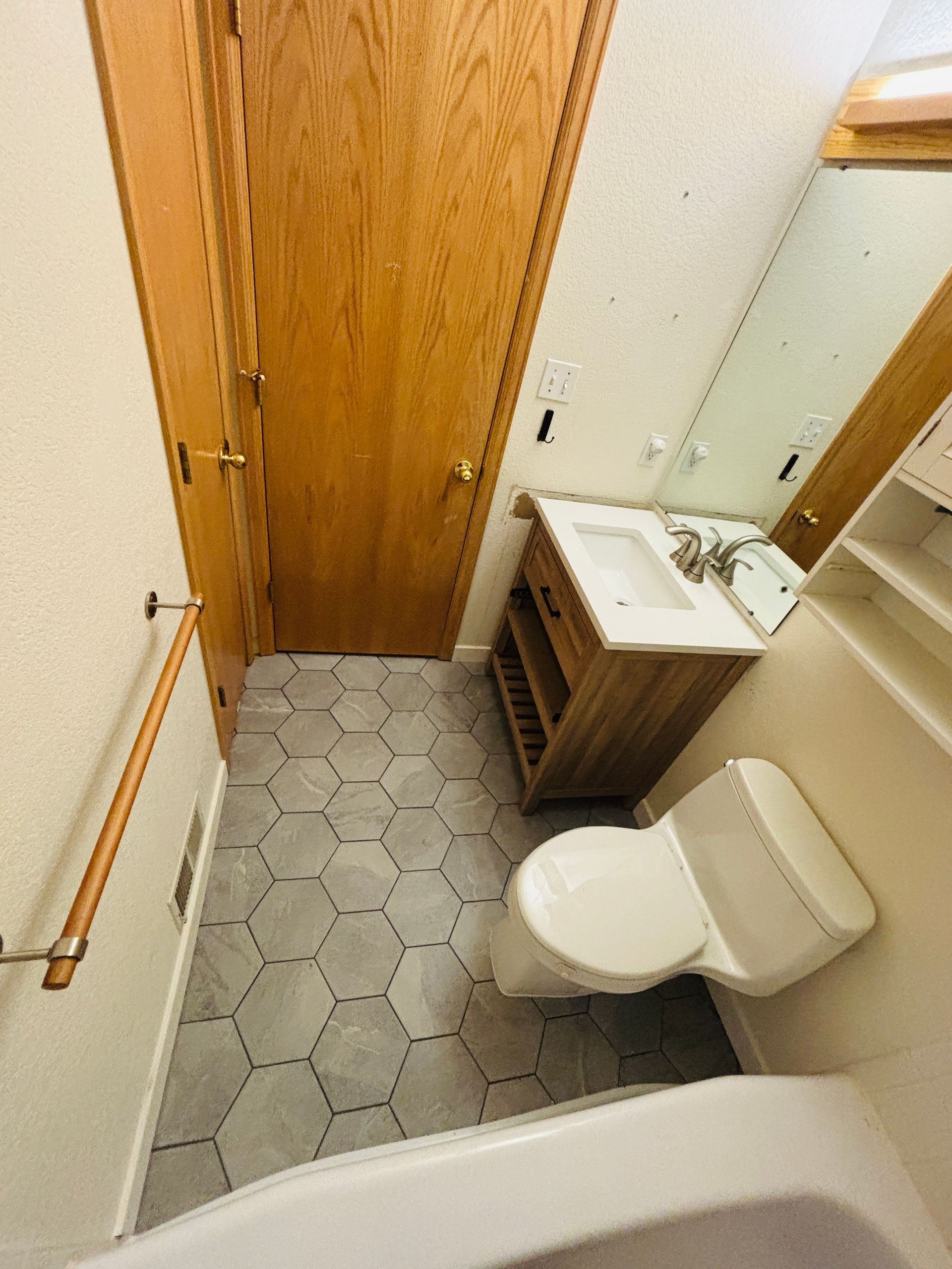 Bathroom with hexagonal tile floor, wooden vanity, toilet, and a closed wooden door.