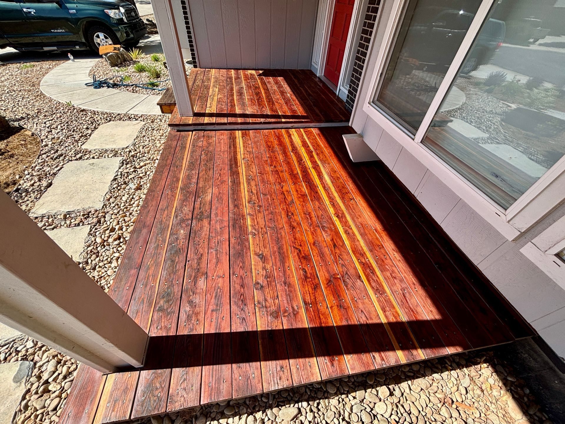 Wooden porch with reddish stain, next to a window and stone walkway.