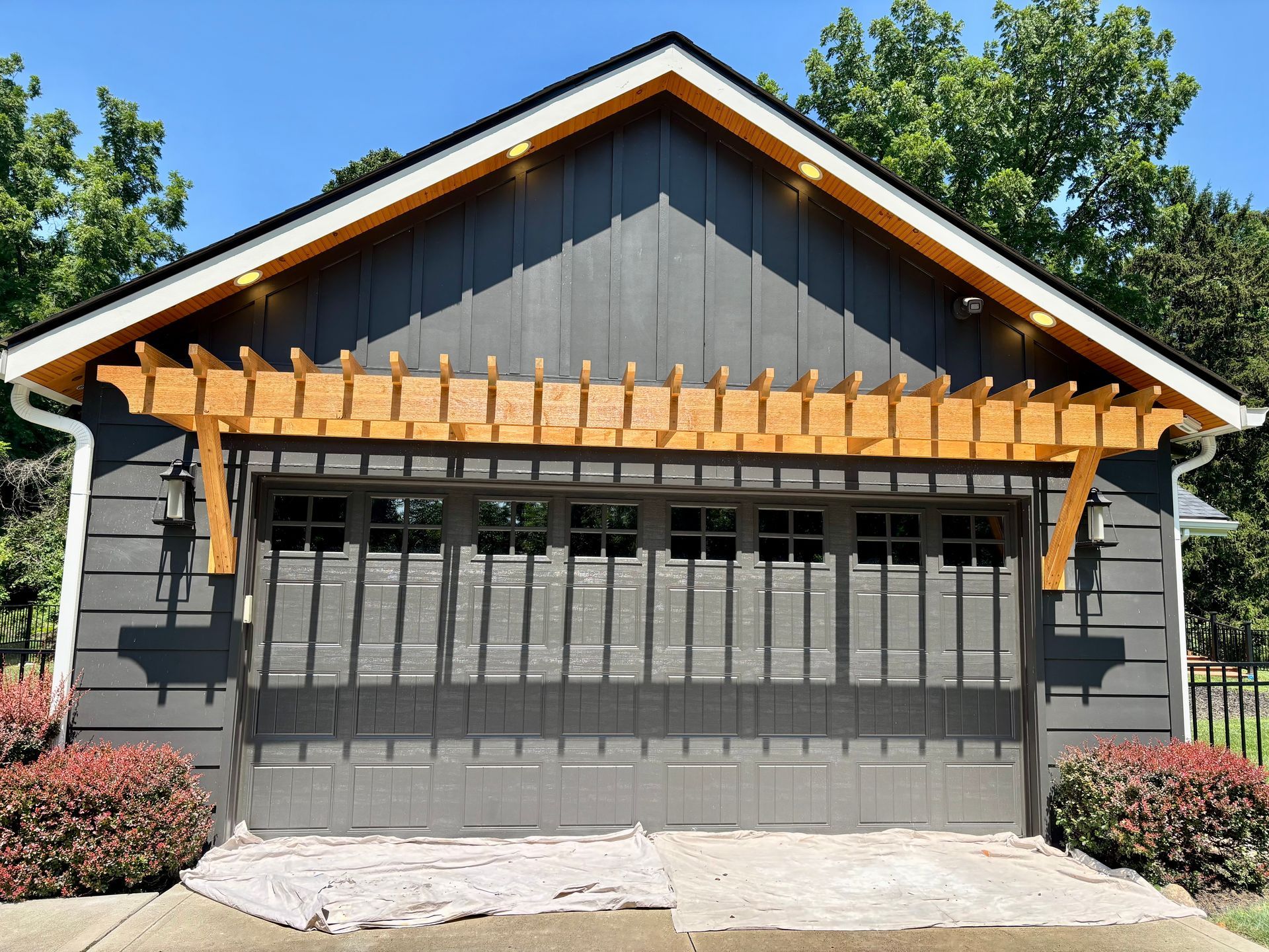 Gray garage with wooden pergola, white trim, and a blue sky.
