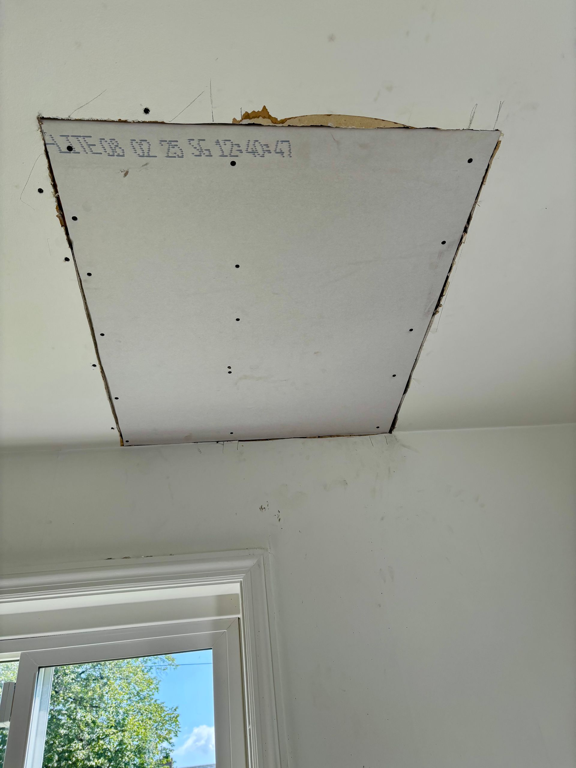Ceiling panel removed, revealing the attic. White walls, window in the lower left corner.