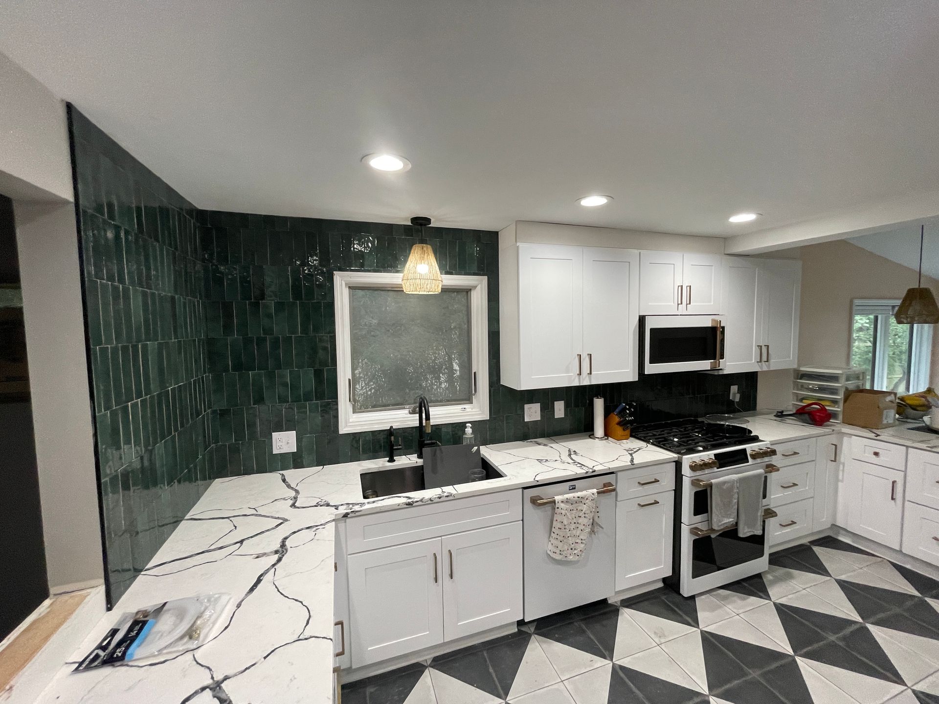Kitchen with white cabinets, dark green tiled wall, black and white countertops, and a black and white tiled floor.