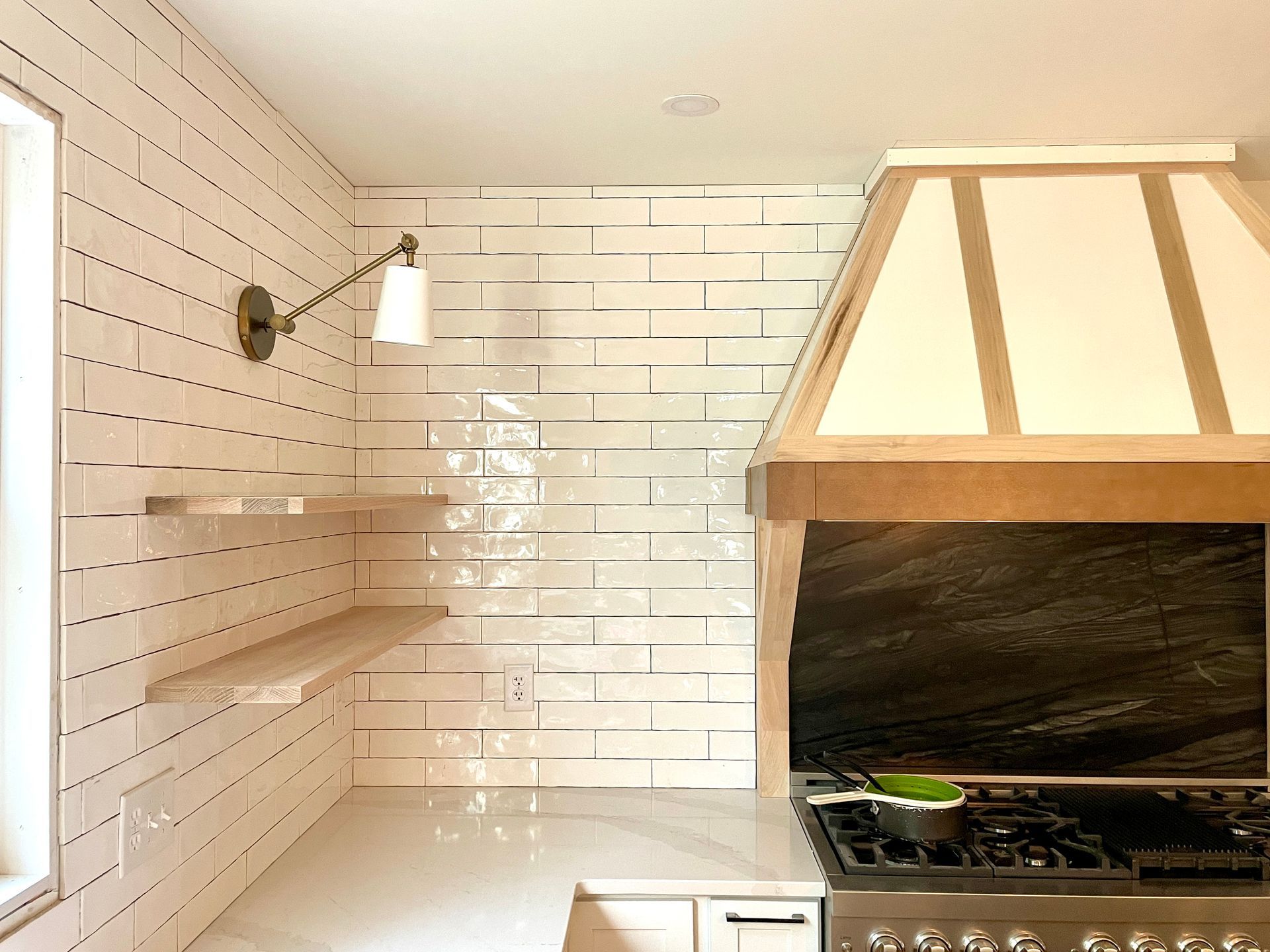 Modern kitchen: white tiled wall with floating shelves, range hood, and stove.