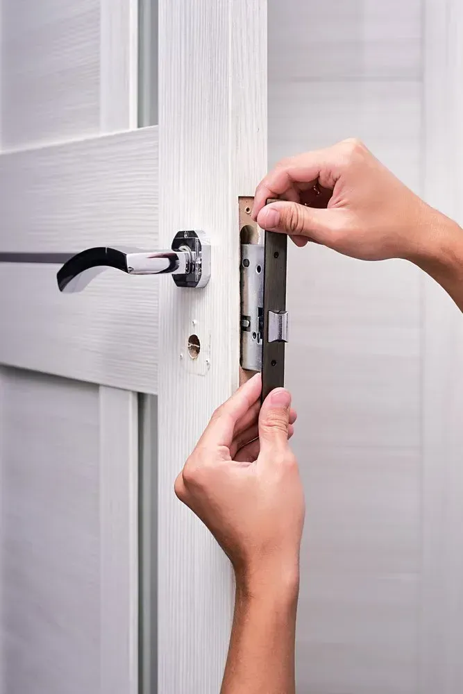Person Installing a Door Latch on a White Door. Hands Holding the Latch, Near Handle — Lady Locksmith in Mackay, QLD
