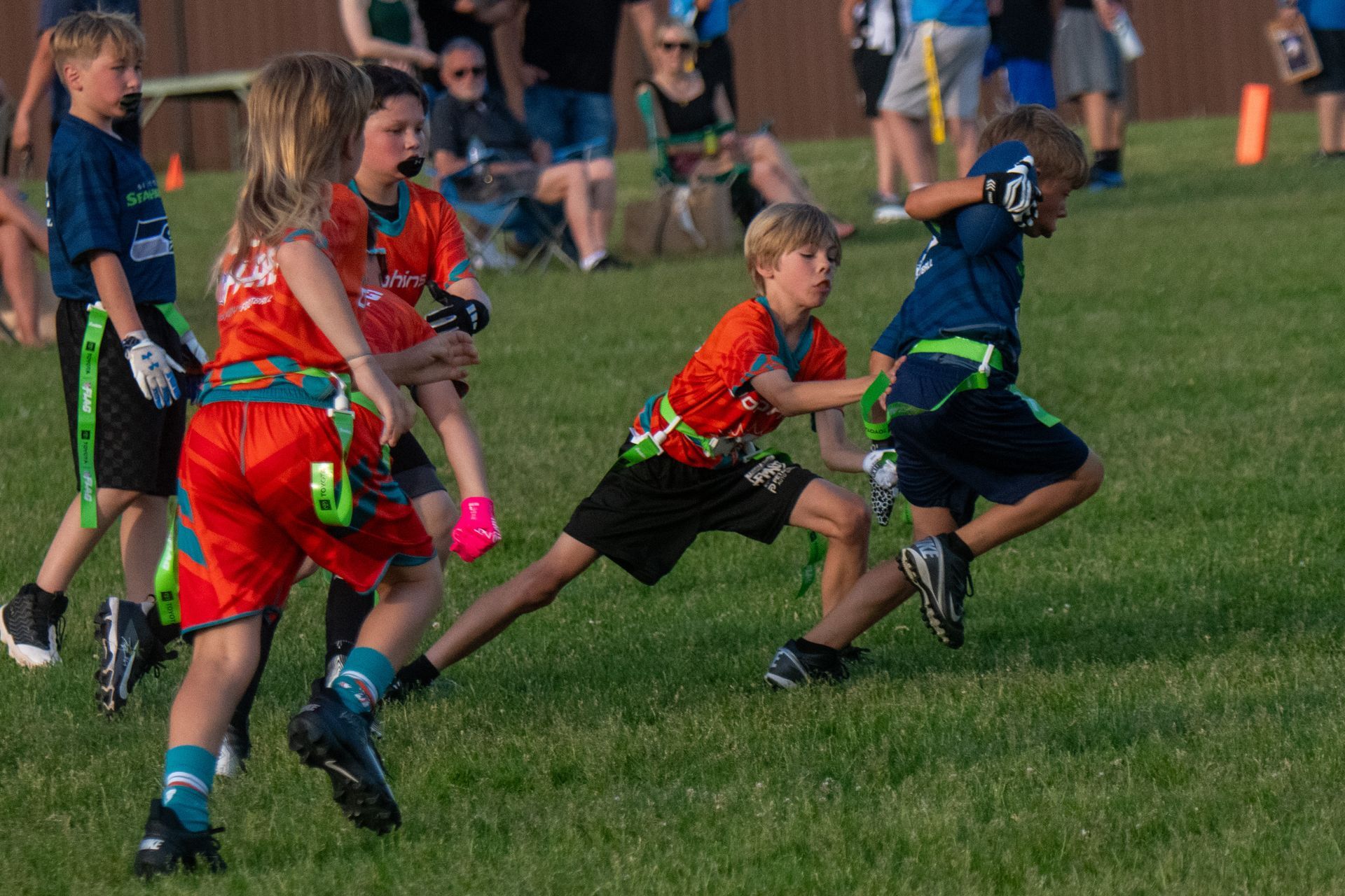 Children in team uniforms playing a flag football game on a grassy field.