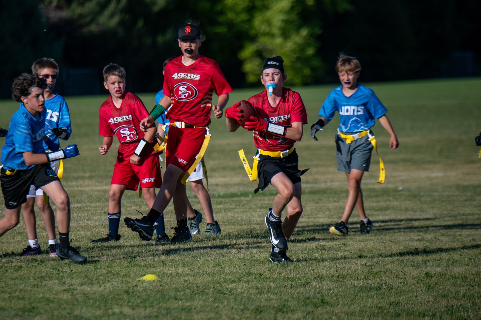 Youth football players in red and blue uniforms running and playing a game on a grass field.