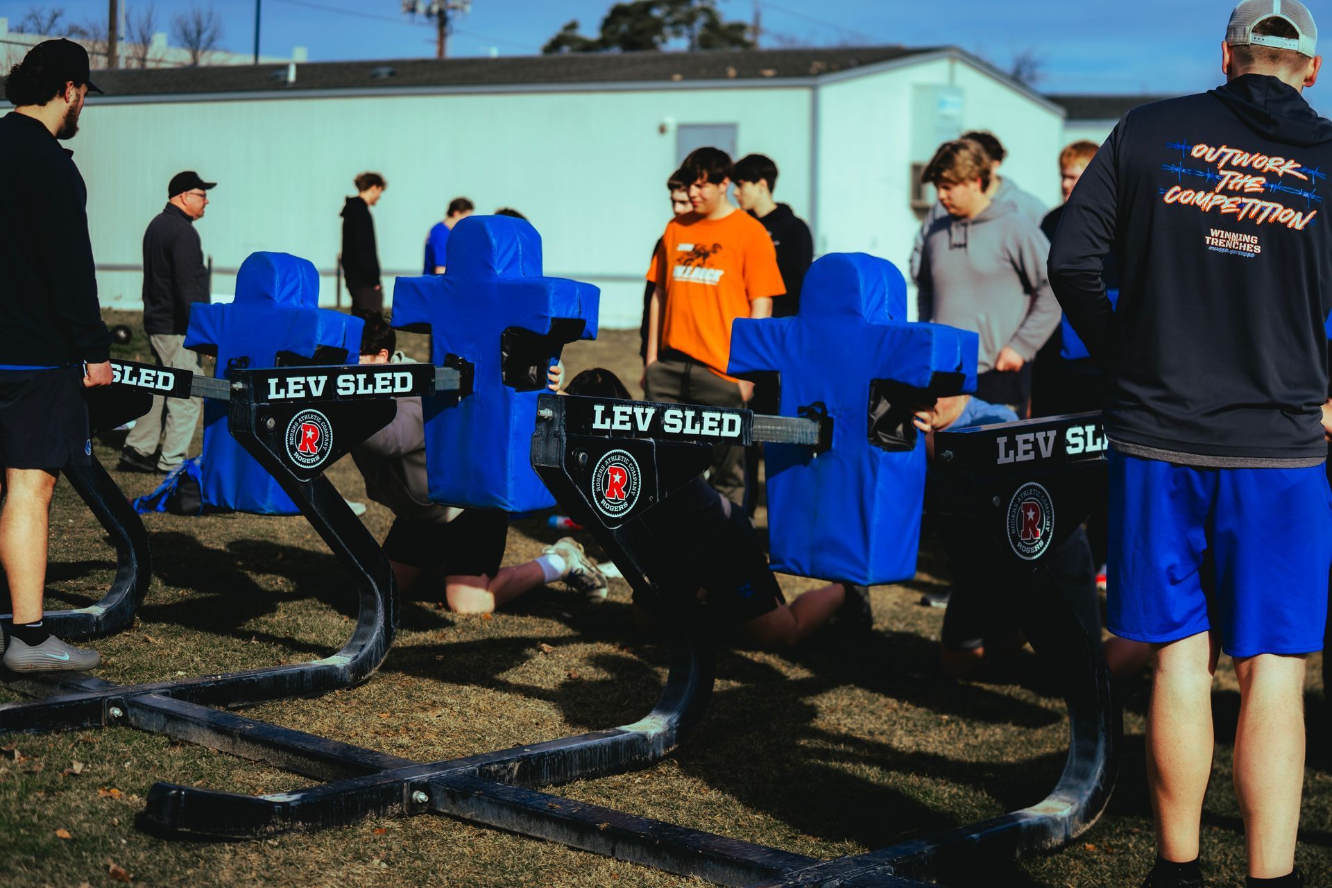 A group of people practicing with blue training sleds on an outdoor field.