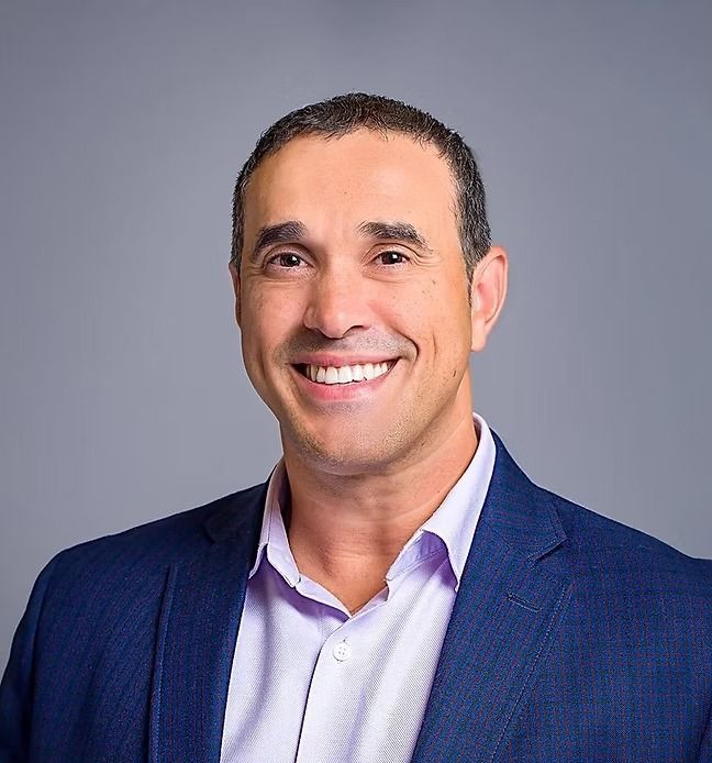 A man in a blue suit and purple shirt is smiling for the camera.