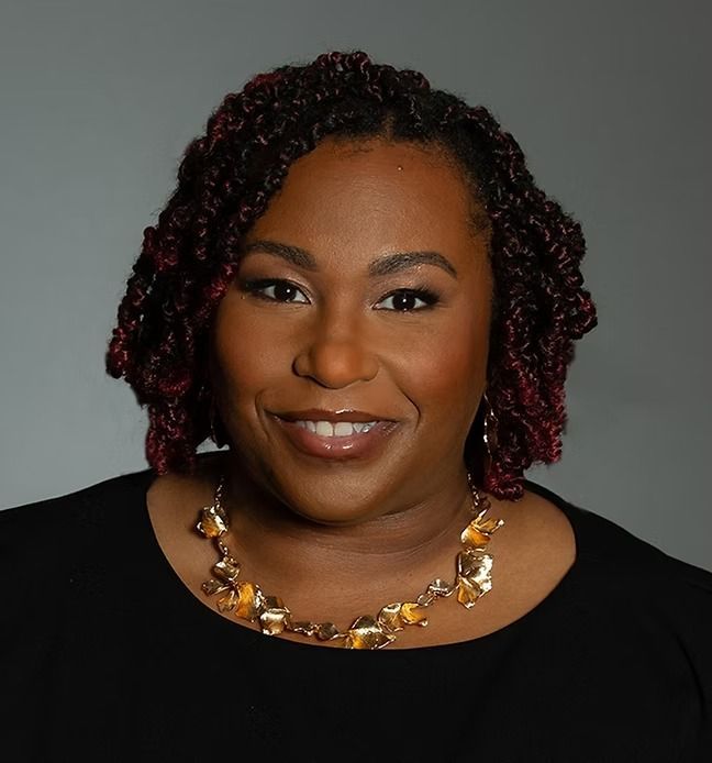 A woman wearing a black shirt and a gold necklace smiles for the camera.