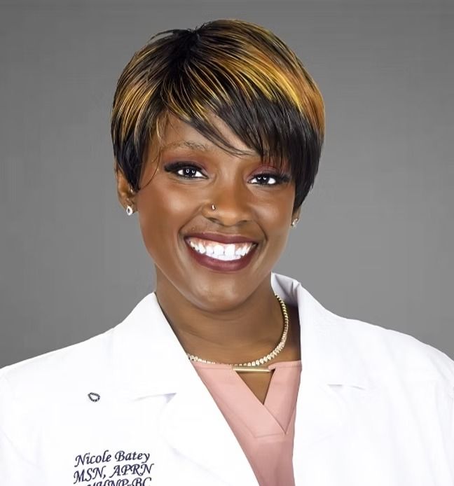 A woman wearing a lab coat with the name nicole baker on it