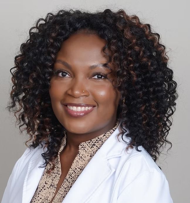A woman with curly hair is wearing a white lab coat