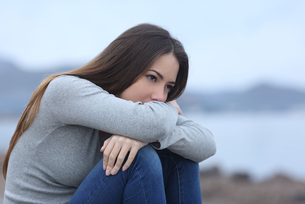 Sad woman sitting on the beach full of anxiety wanting anxiety-relieving hypnotherapy services