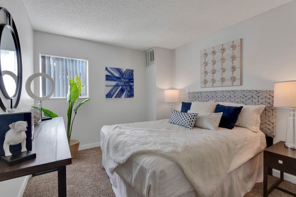 Bright modern bedroom with a bed, blue accents, wall art, and a window with a white blind
