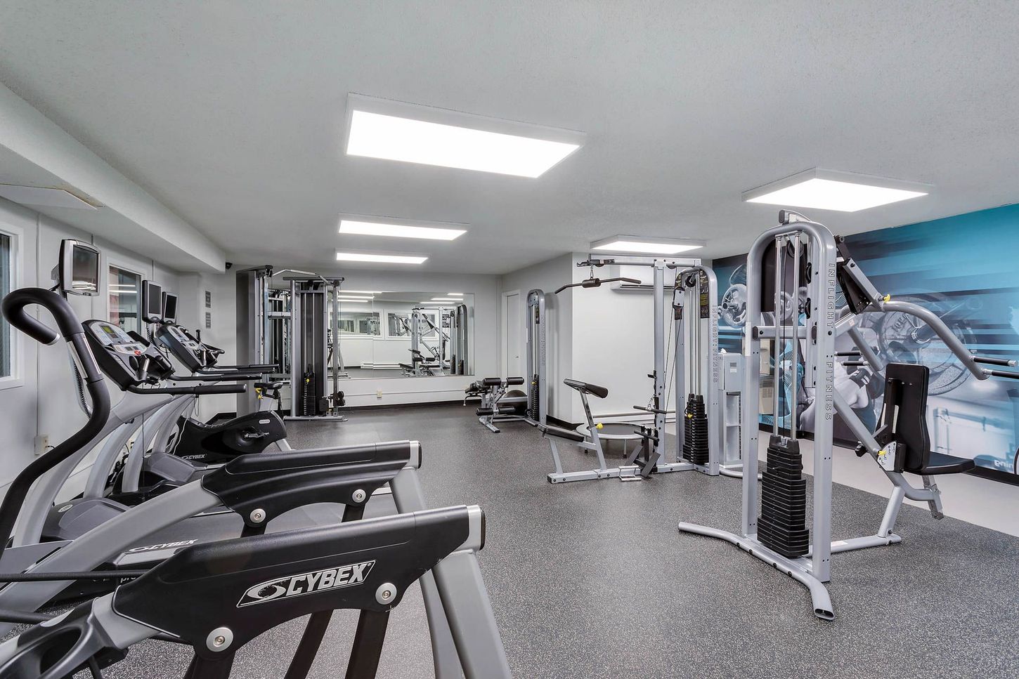 Empty modern gym with treadmills, cable machines, mirrors, and bright overhead lights