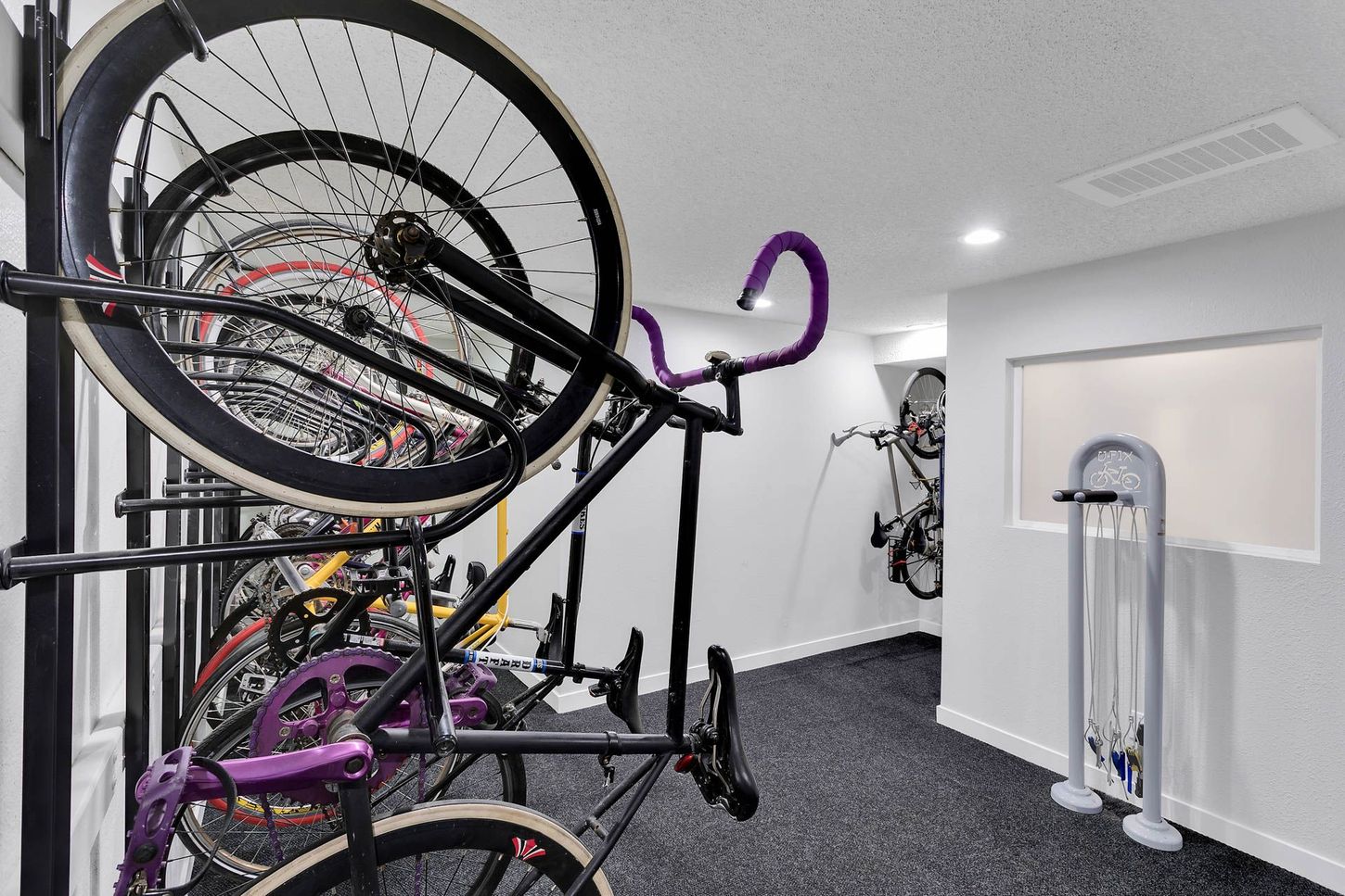 Bicycles stored on wall-mounted racks in a bright indoor room with carpet and white walls