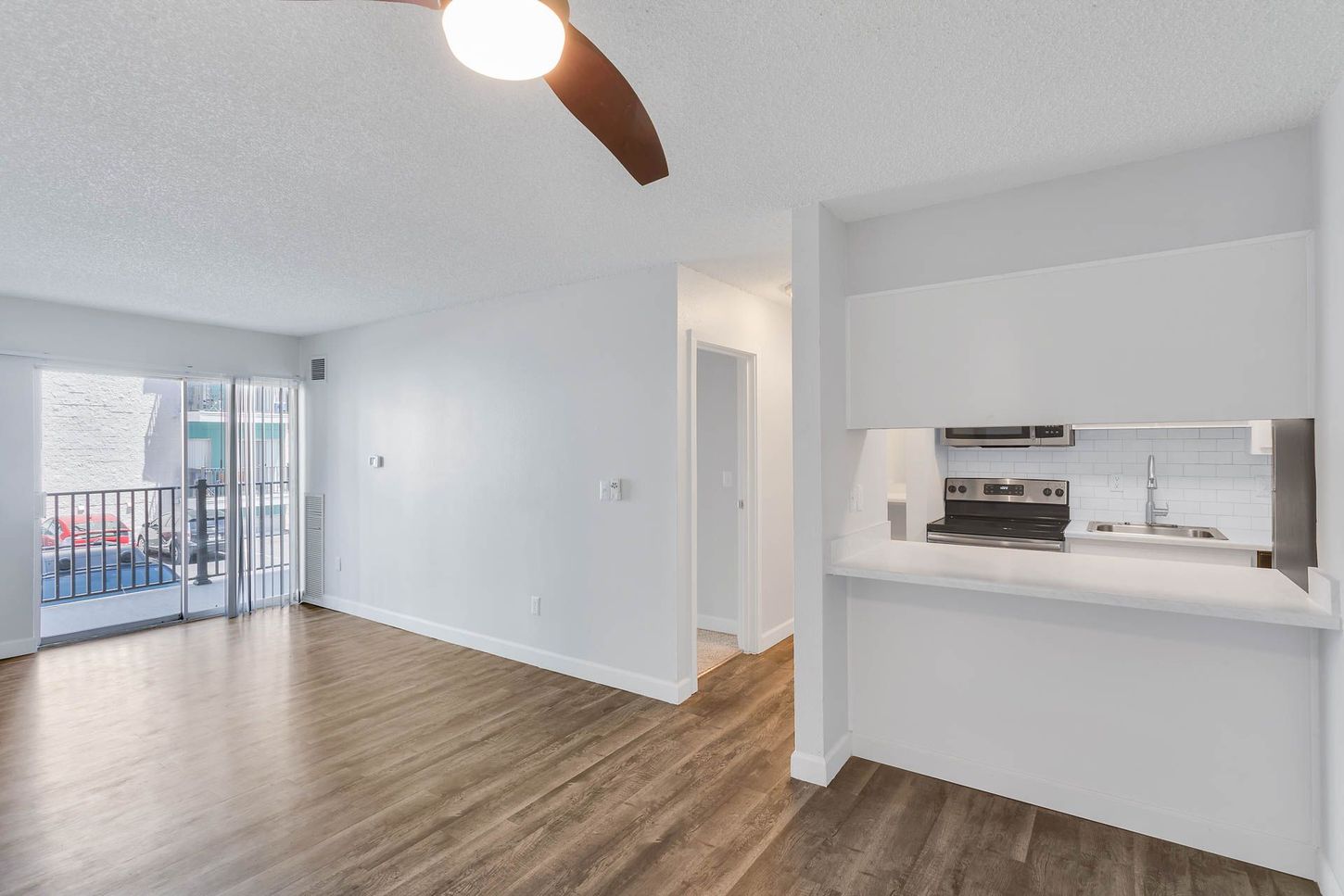 Empty open-plan living room with wood floors, ceiling fan, and kitchen pass-through window