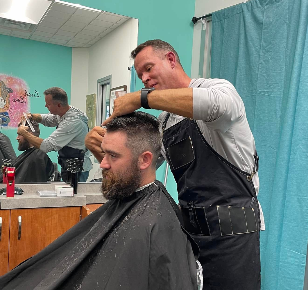 Barber performing a men's haircut in a barbershop, providing precision cutting services for a bearded client.