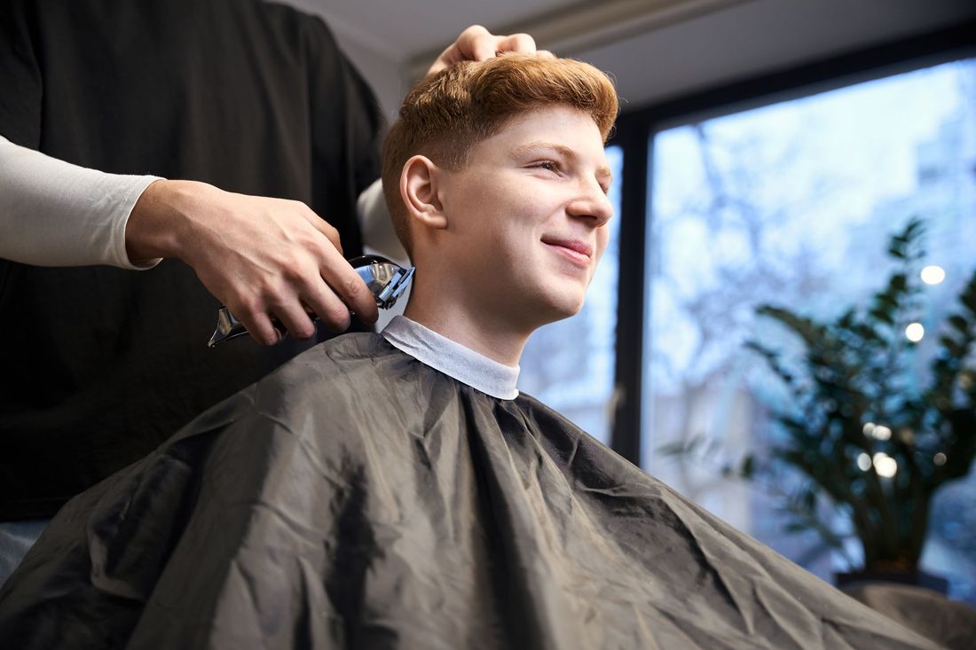 Teen client getting a fresh taper fade haircut in a barbershop, showcasing a clean, modern men's hairstyle in progress.
