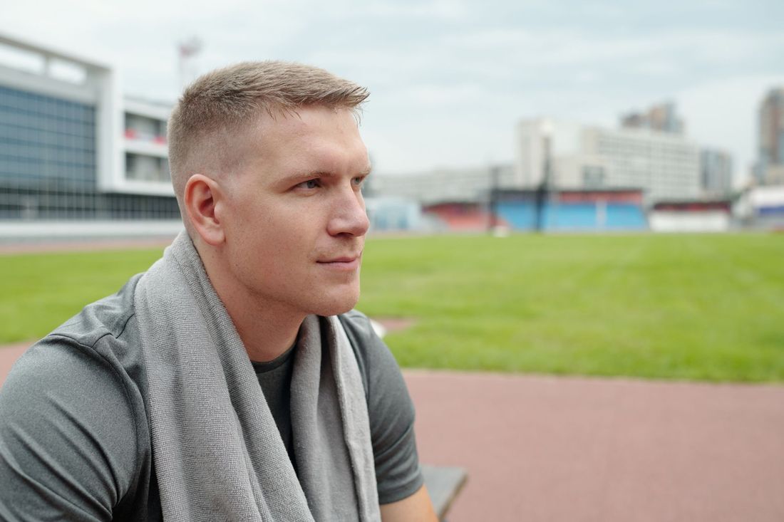 Man with a fresh buzz cut sitting near a baseball field, showcasing a clean tapered fade and athletic men's haircut style.