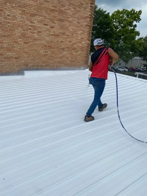 Technician spray-applying reflective coating to a commercial roof