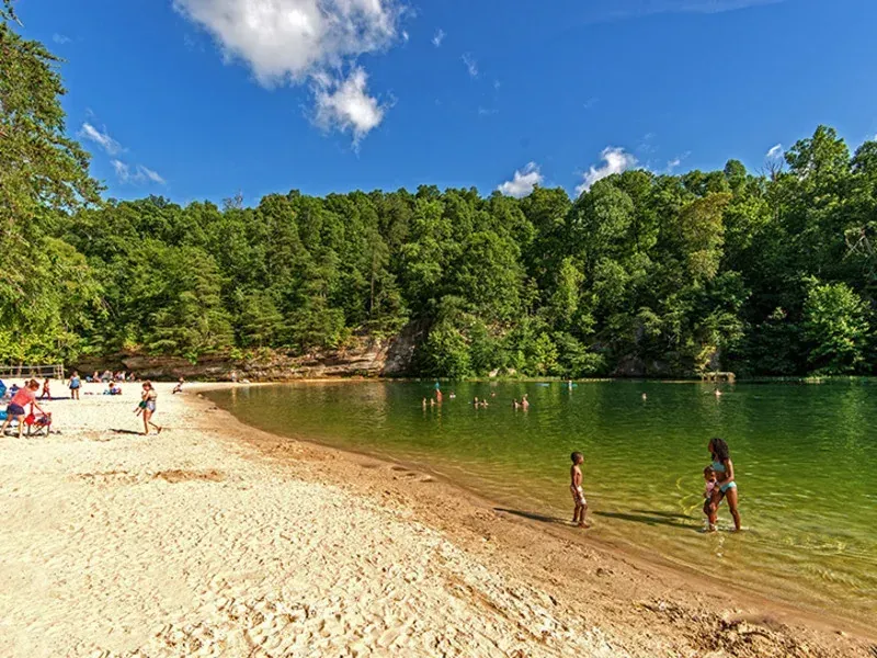 Sandy swimming beach at Pennyrile Forest State Resort Park in Dawson Springs, Kentucky, with families swimming in the green lake water surrounded by wooded hills