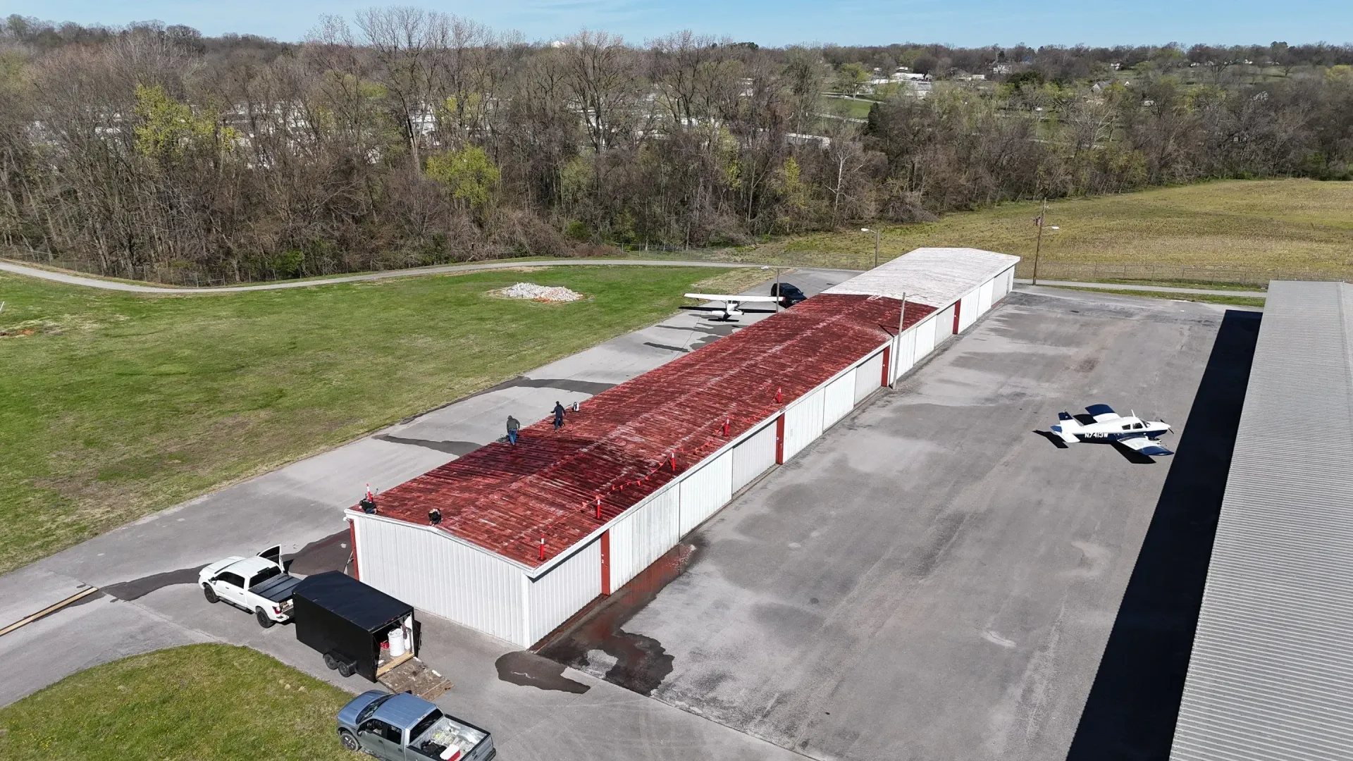 Aerial view of metal roof restoration in progress, showing completed white sections alongside untreated rusted sections in Hopkinsville, Kentucky