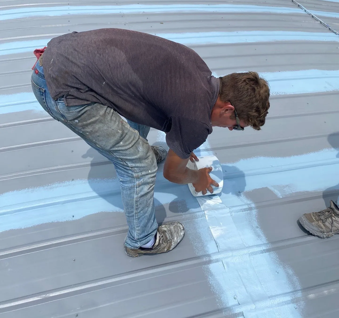 Technician applying coating along a seam detail on a curved metal commercial roof