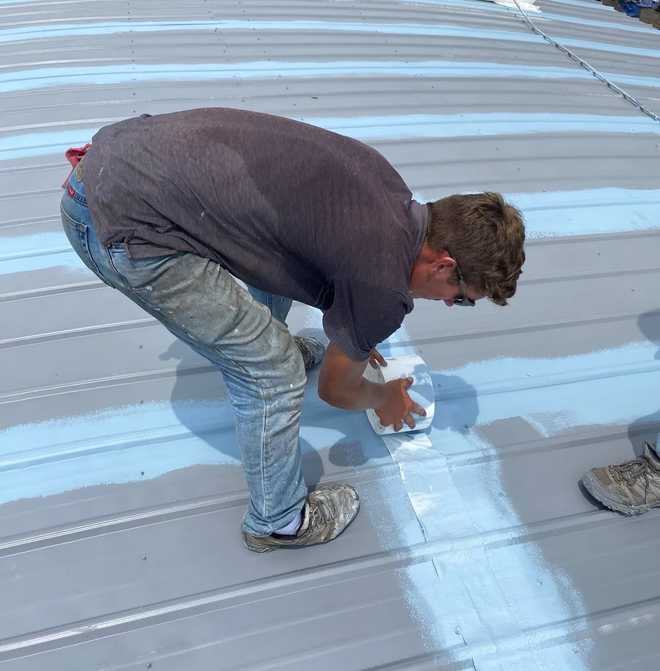 Technician applying coating along a seam detail on a curved metal commercial roof