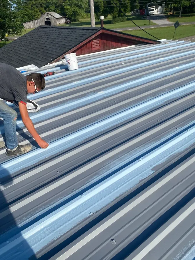 Technician applying primer and topcoat along metal roof seams during restoration