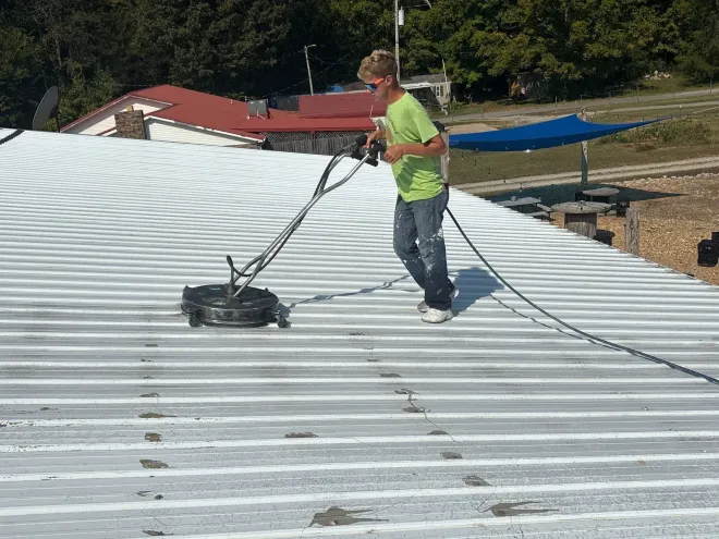 Technician using a rotary surface cleaner on a commercial metal roof during a maintenance visit