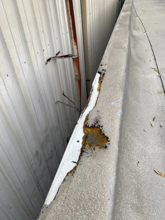 Failed metal edge flashing exposing rusted substrate on a commercial flat roof parapet