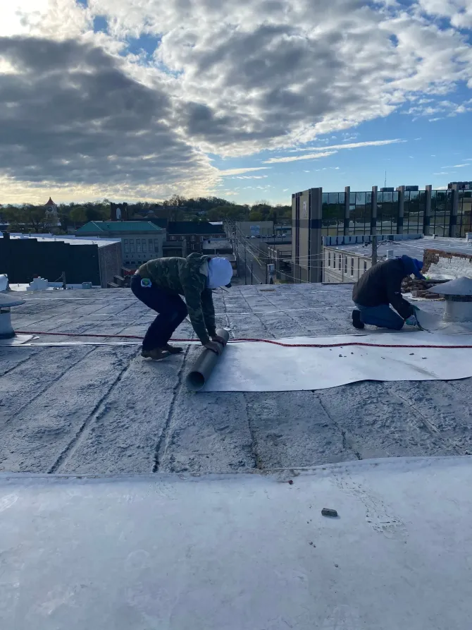Crew rolling out single-ply membrane roofing over insulation board during installation