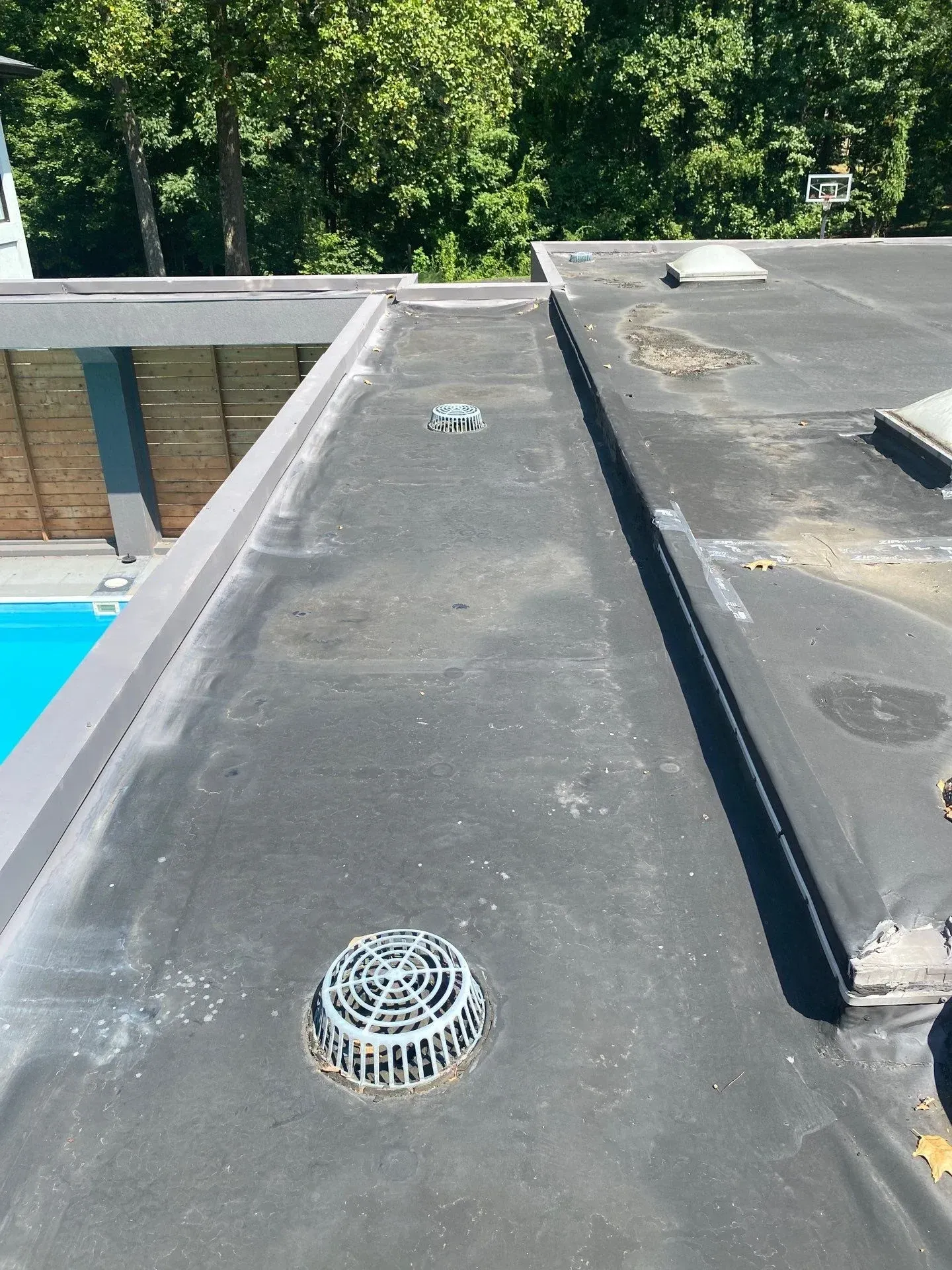 Weathered flat roof membrane with repair patch near a roof drain on a residential property