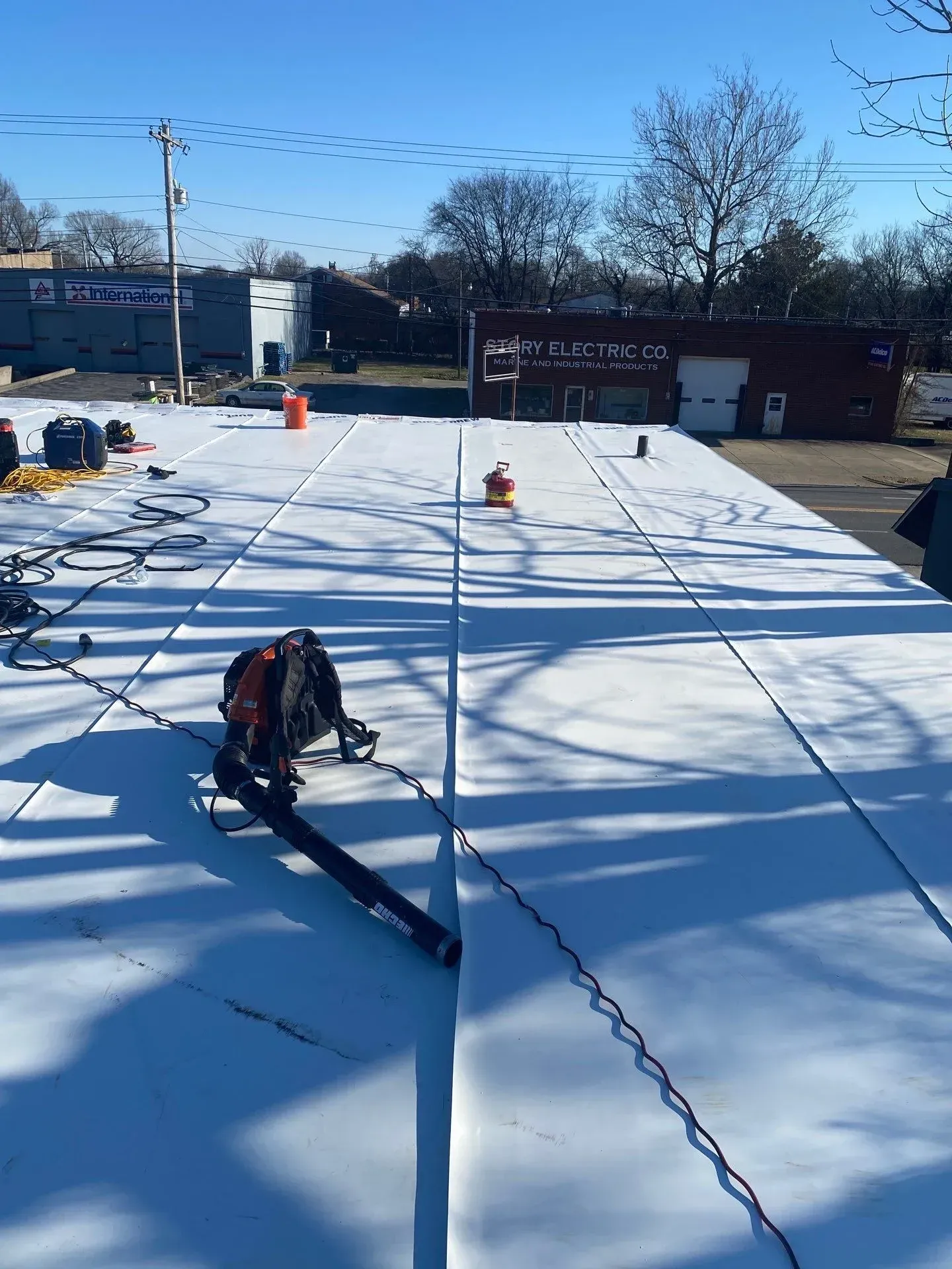 Completed white TPO membrane roof installation with cleanup equipment on a commercial building