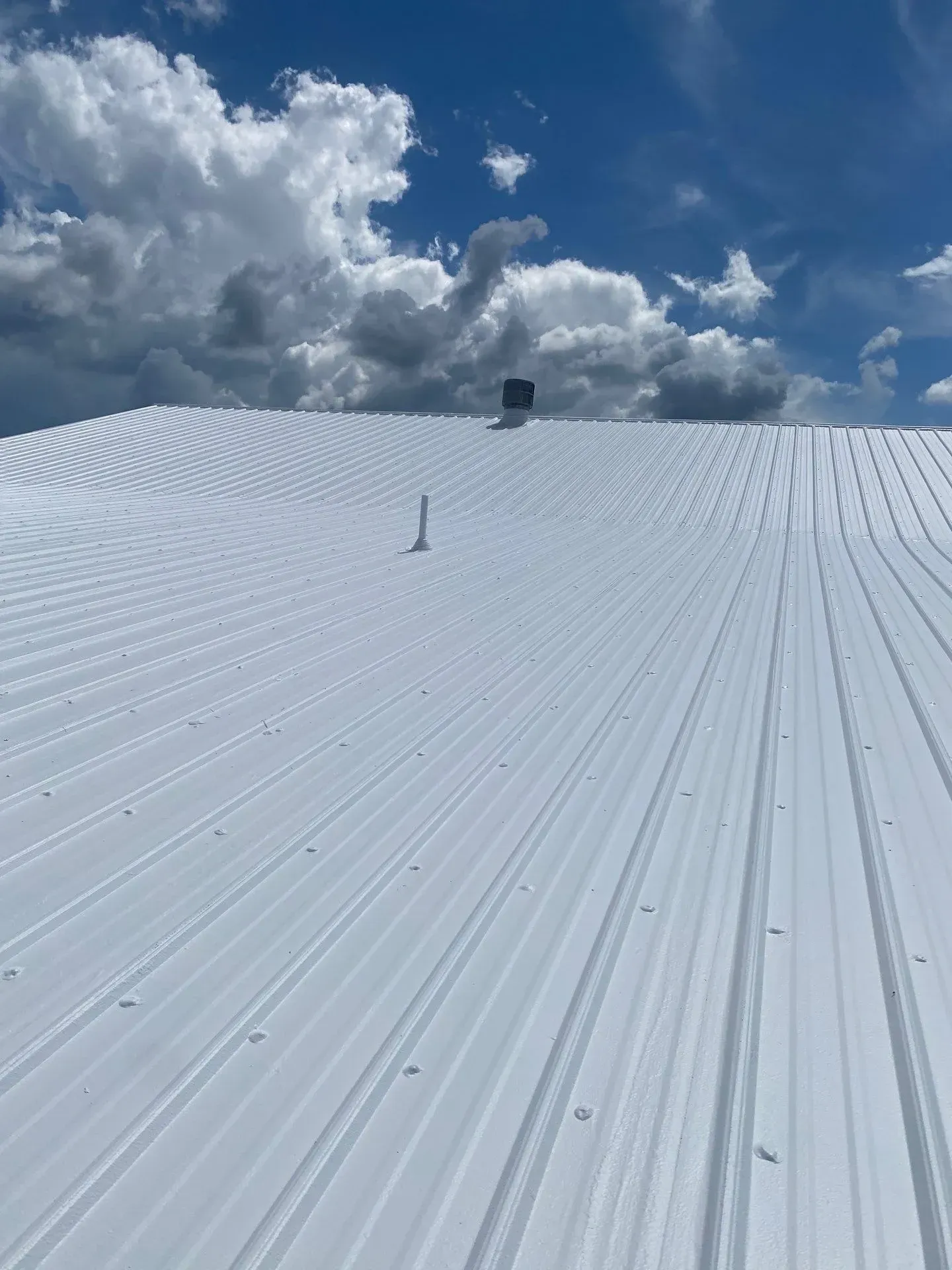 White reflective commercial metal roof coating under a Kentucky sky with storm clouds
