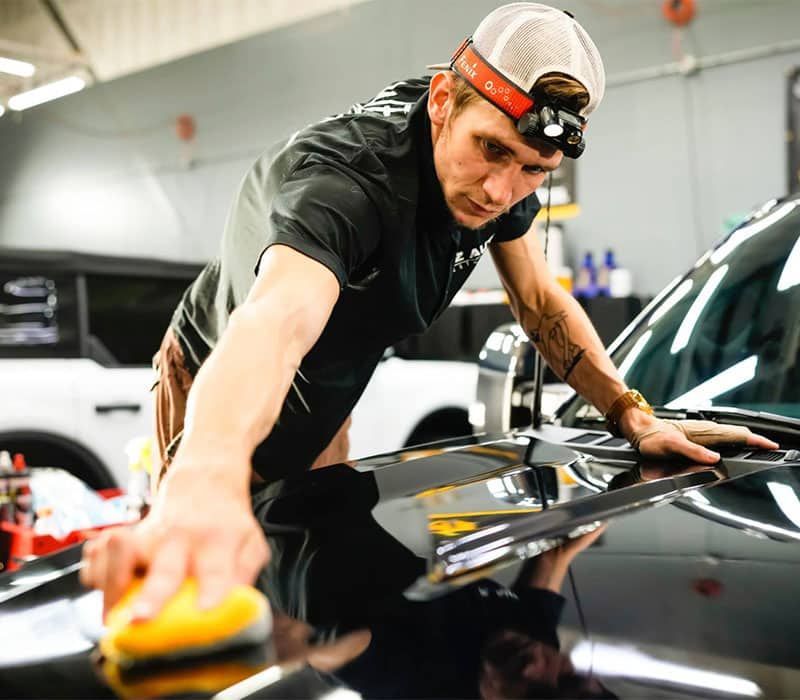A man is polishing a black car with a yellow sponge.