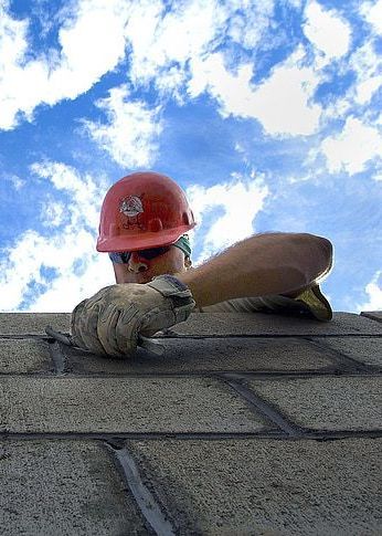 A man wearing a hard hat and gloves is working on a brick wall.