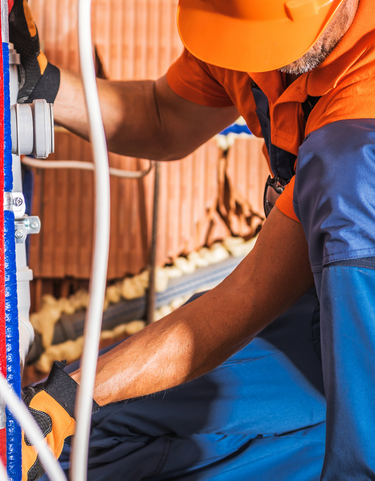 A man wearing an orange hard hat is working on a pipe