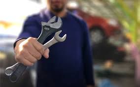 A man is holding a wrench in his hand in front of a car.