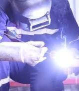 A man wearing a welding helmet is welding a piece of metal.