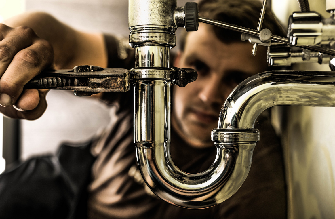 A man is fixing a pipe with a wrench.