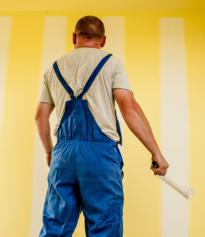 A man in blue overalls is painting a yellow and white striped wall