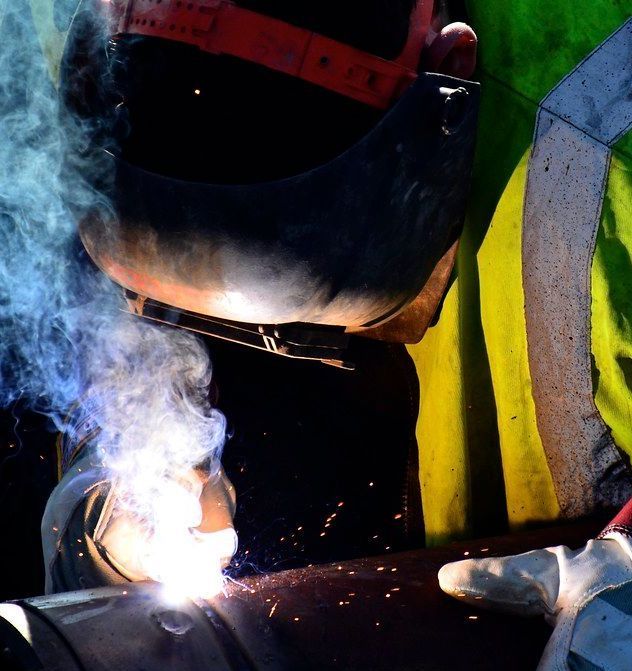 A man wearing a welding mask is welding a pipe