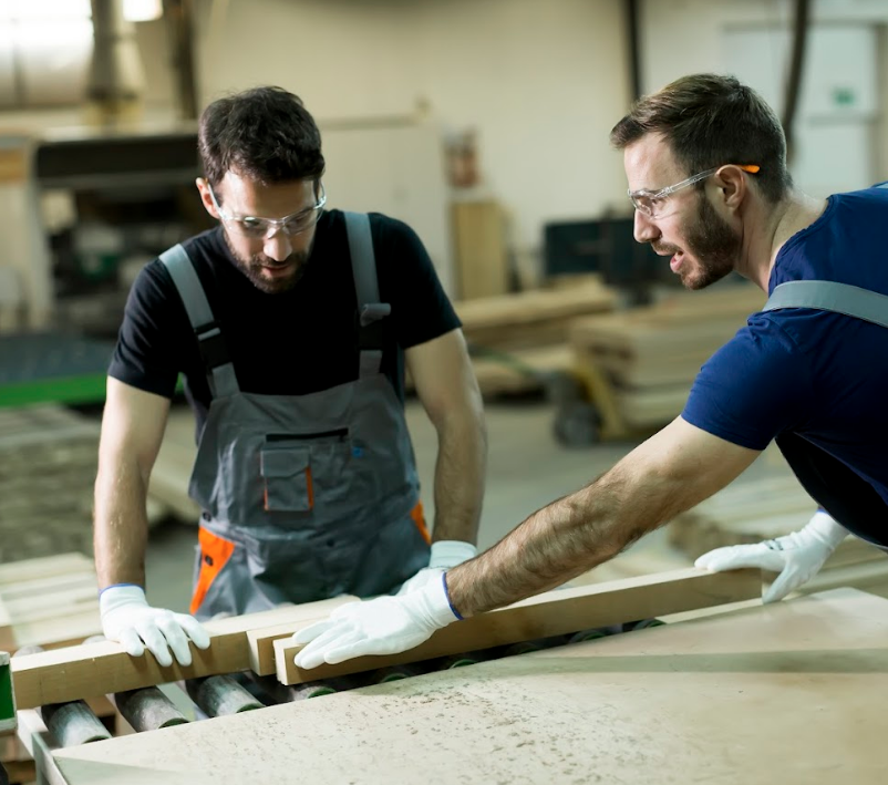 Two men are working on a piece of wood in a factory.
