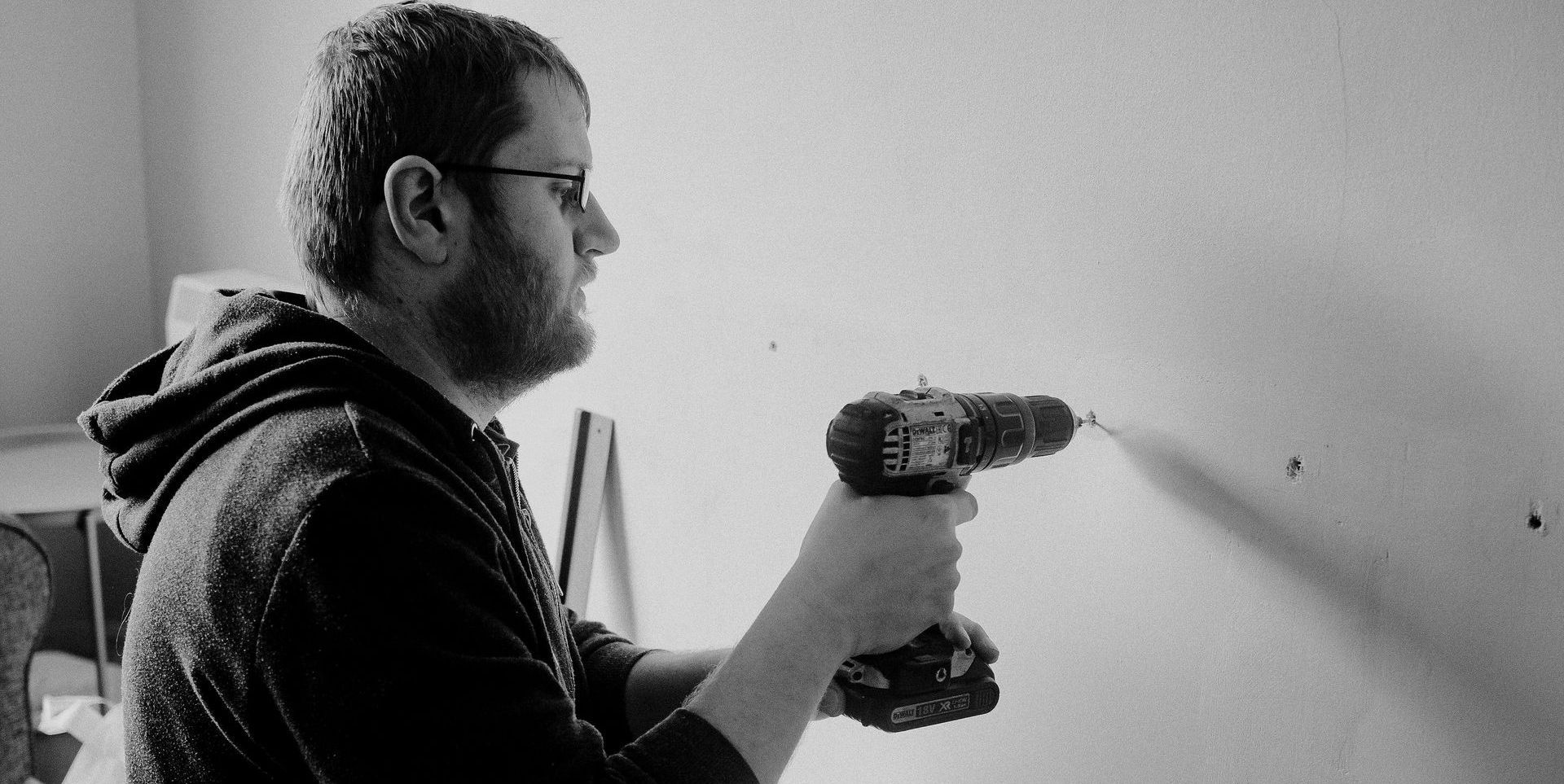 A man is using a drill on a wall in a black and white photo.