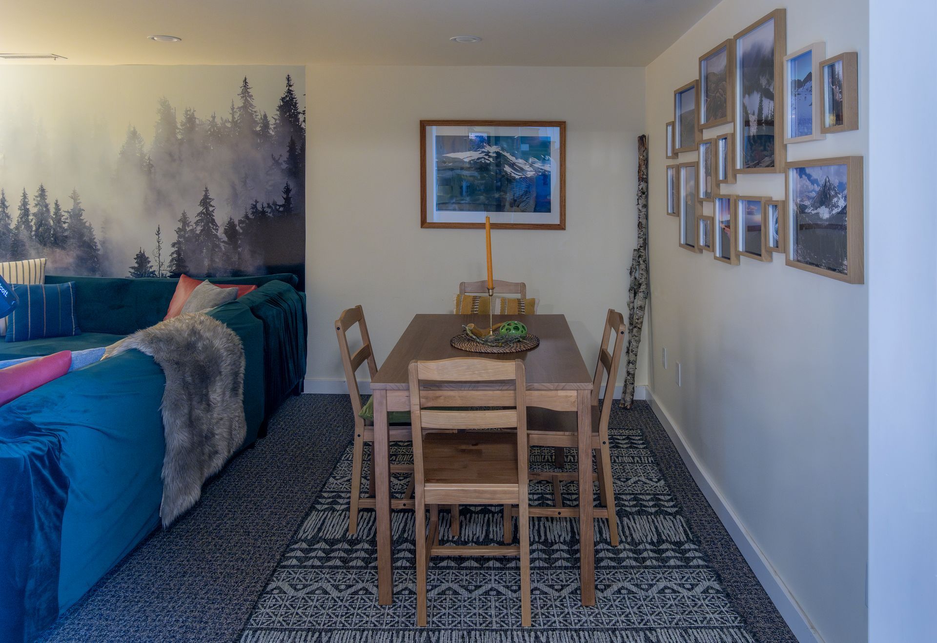 Dining area with wooden table and chairs in a narrow room, patterned rug, framed art, and sofa along the left wall