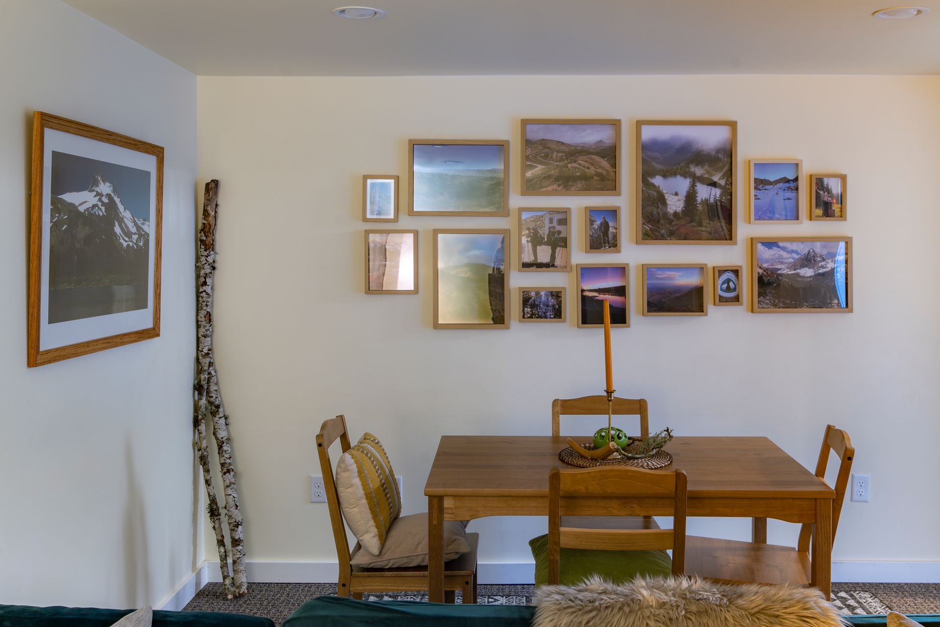 Dining nook with wooden table and chairs beneath a gallery wall of framed landscape photos
