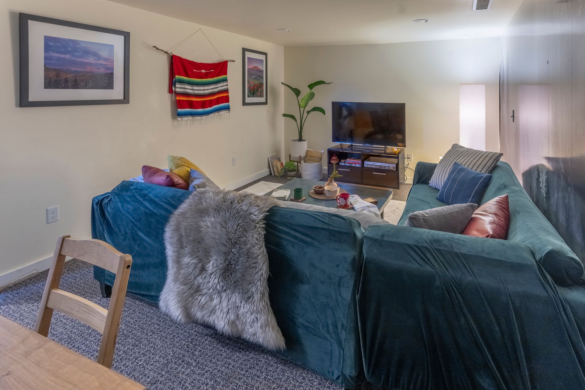 Living room with teal sectional sofa, TV, wall art, and colorful blanket on the wall