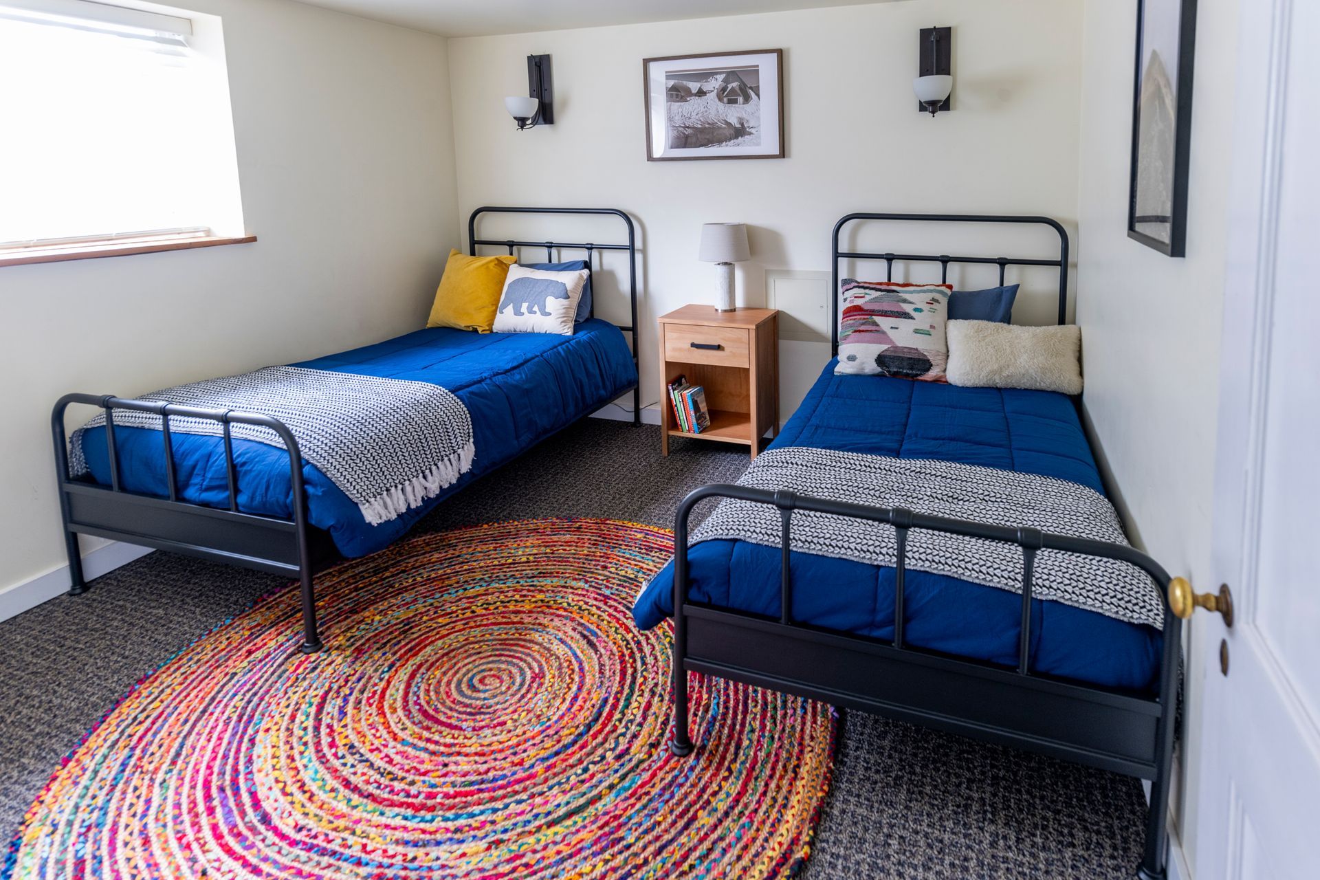 Bedroom with two blue twin beds, colorful round rug, and a small nightstand between them